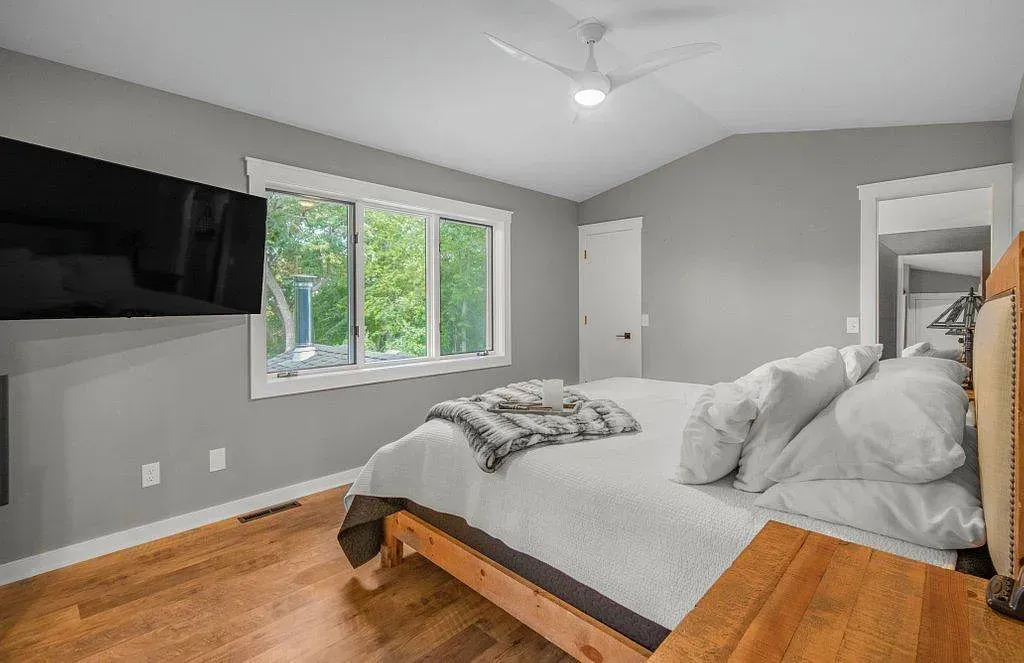 Bright bedroom with a large bed, wall-mounted TV, window, and light gray walls.