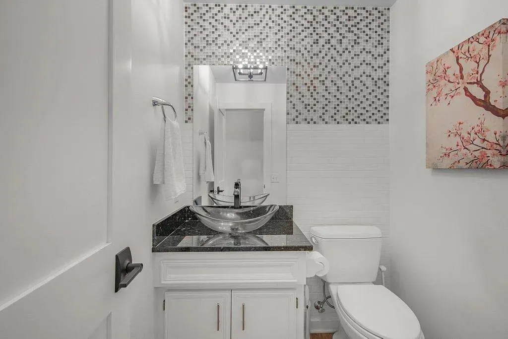 Small white bathroom with black vanity, mosaic backsplash, mirror, and toilet.