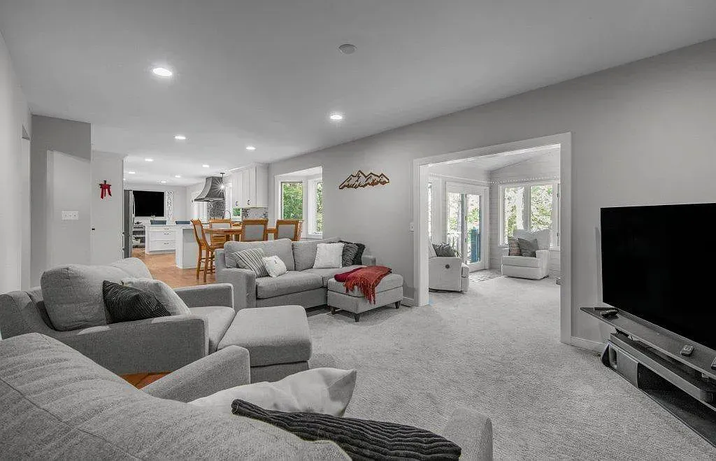 Bright open-plan living room with gray sofas, fireplace, large TV, and glass doors to a patio.
