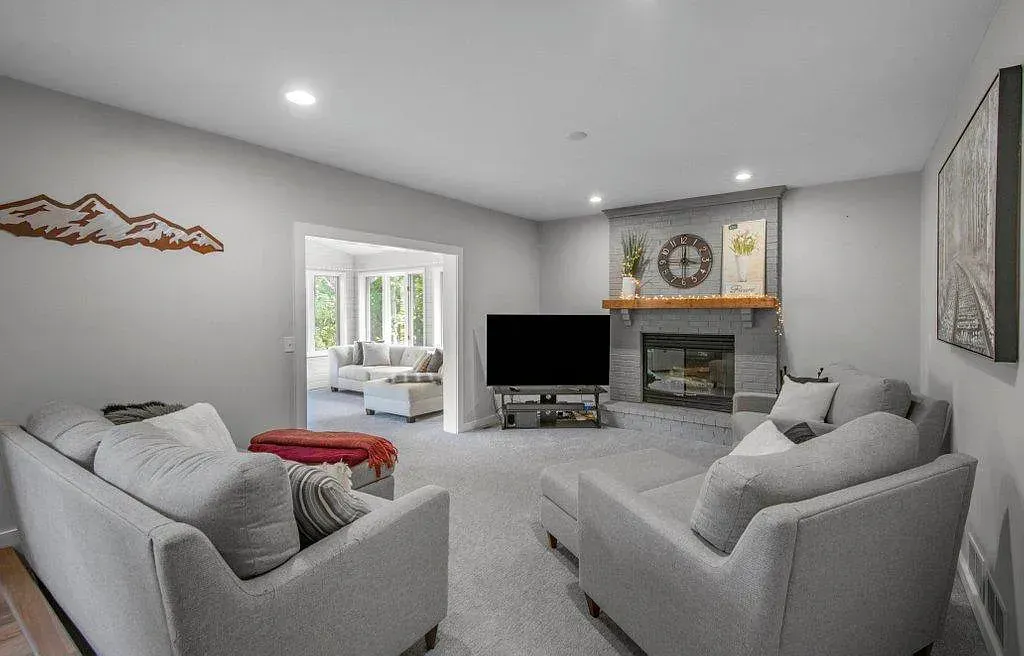 Bright living room with gray sofas, fireplace, TV, and French doors to a sunroom
