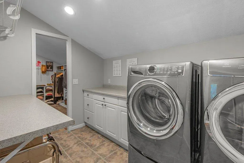 Laundry room with front-loading washer and dryer, white cabinets, and tiled floor alongside a countertop.