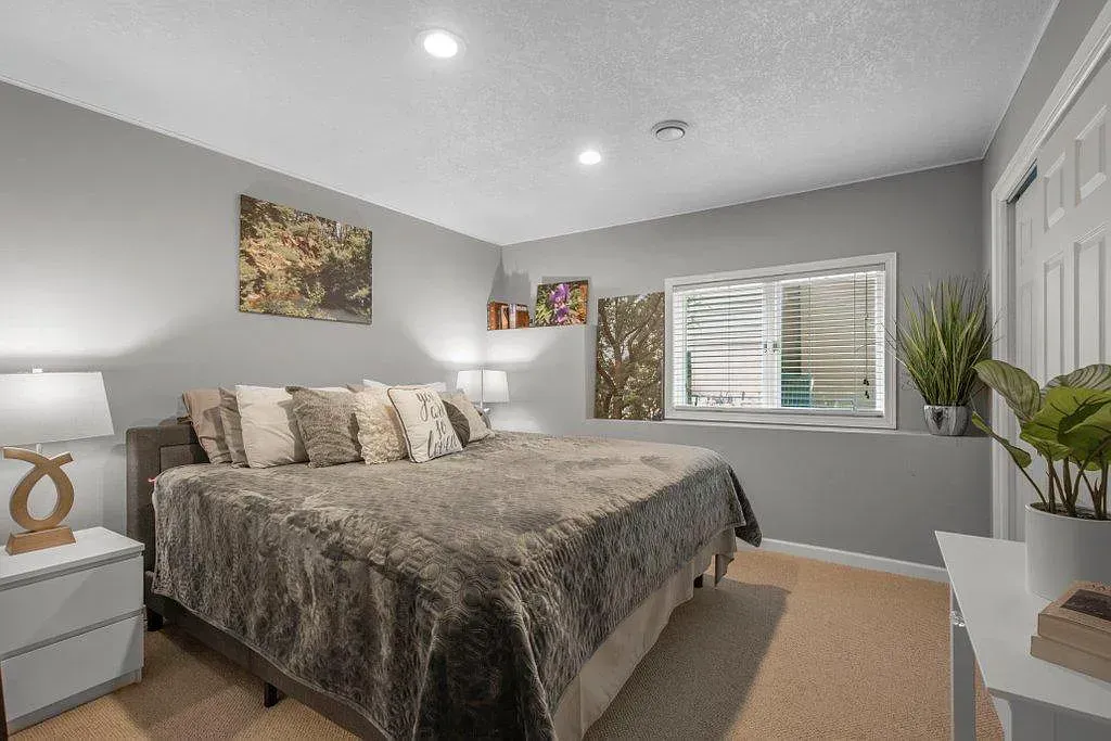 Modern bedroom with a large bed, gray walls, white dresser, and window with blinds