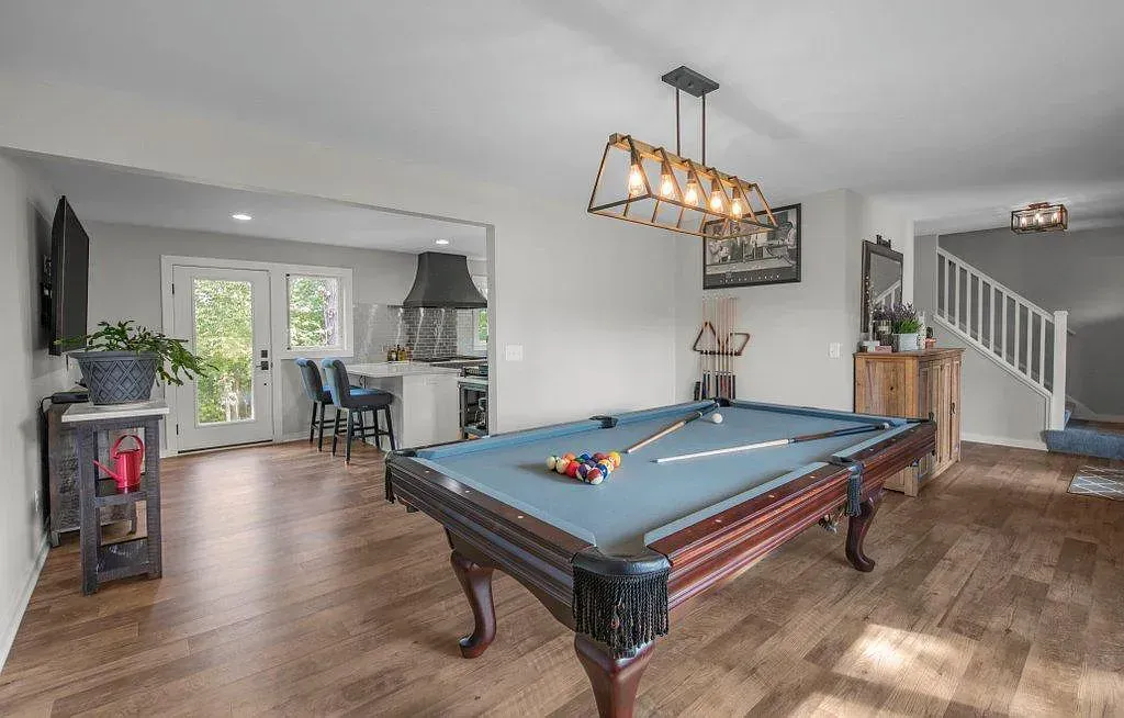 Spacious game room with pool table, chandelier, fireplace, and staircase, in neutral tones.