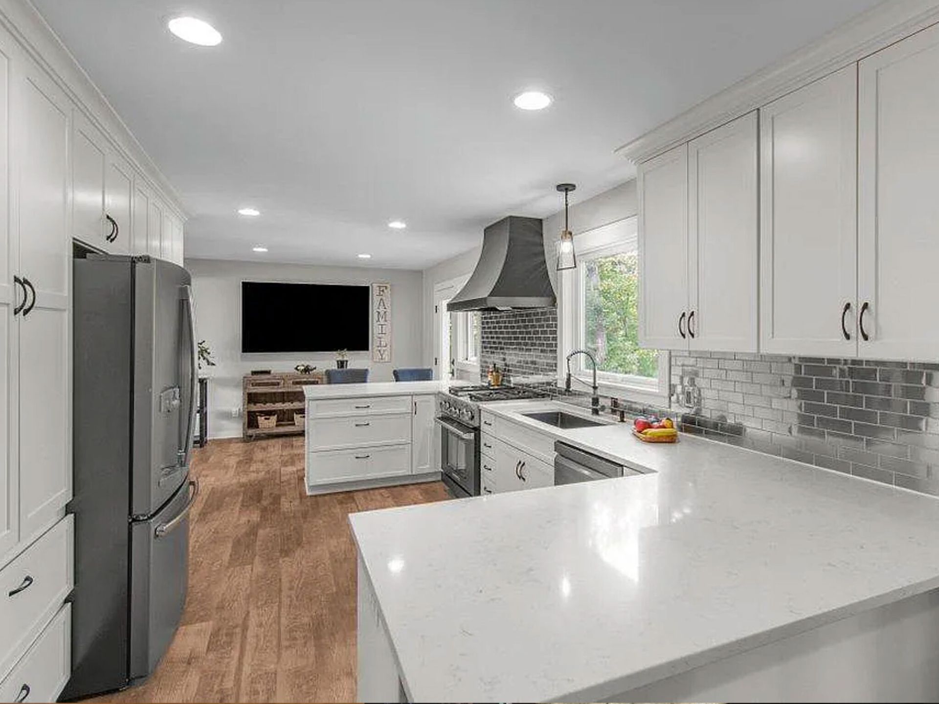 Bright modern kitchen with white cabinets, gray fridge, island, tile backsplash, and hardwood floor