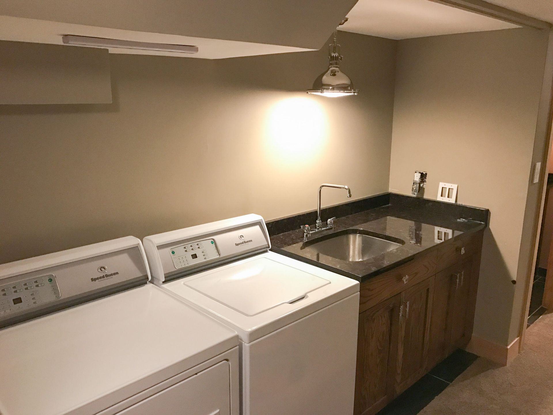 Laundry room with washer, dryer, utility sink, and cabinets under a wall light.