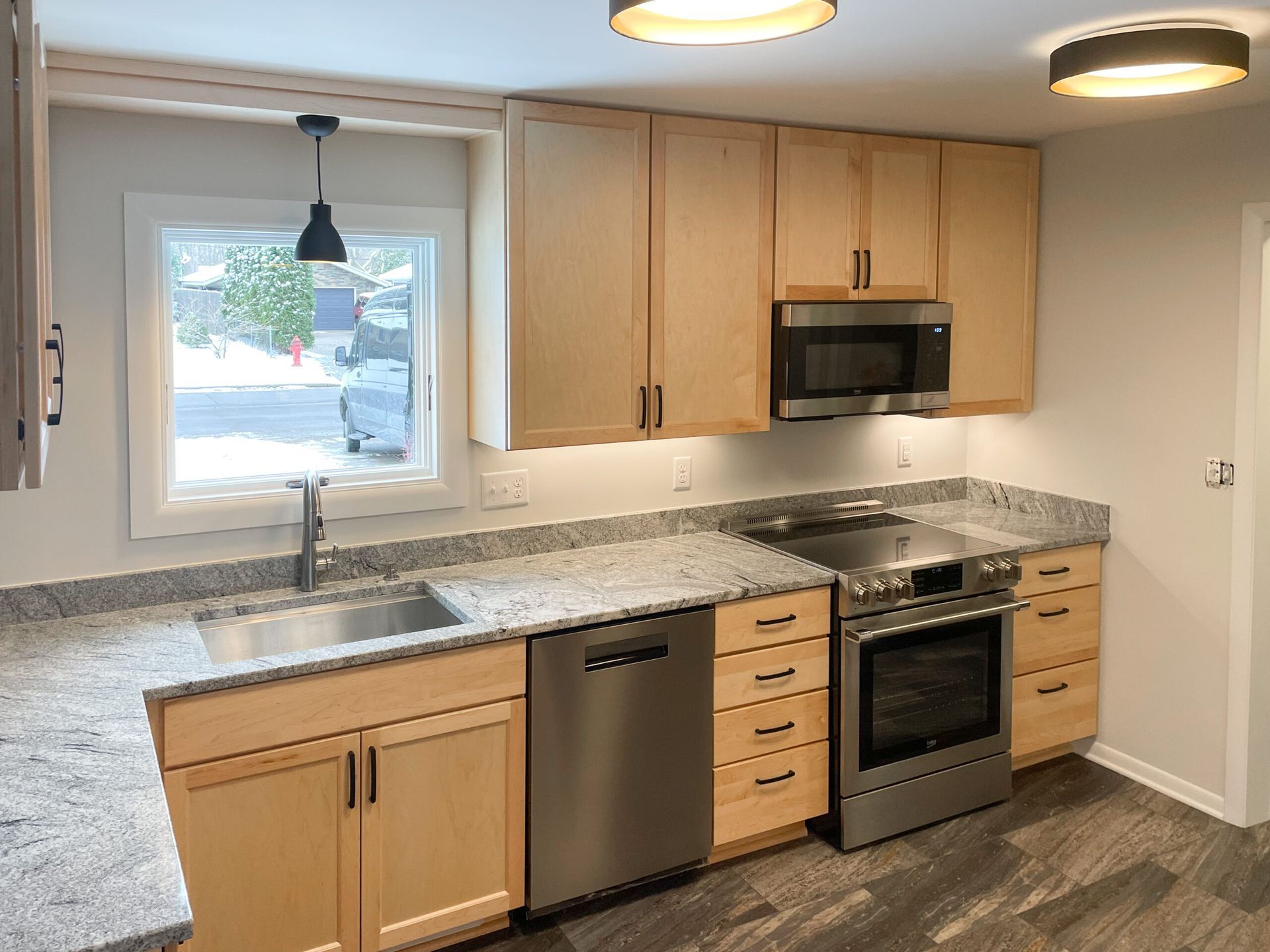 Modern kitchen with light wood cabinets, granite countertop, stainless appliances, and a window over the sink