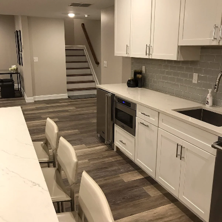 Modern kitchen island with granite countertop, double sink, and wooden staircase in the background