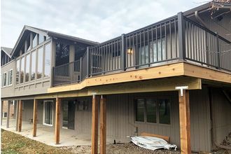 Two-story house under construction with gray siding, wooden deck, and black railings Two-story house under construction with gray siding, wooden deck, and black railings