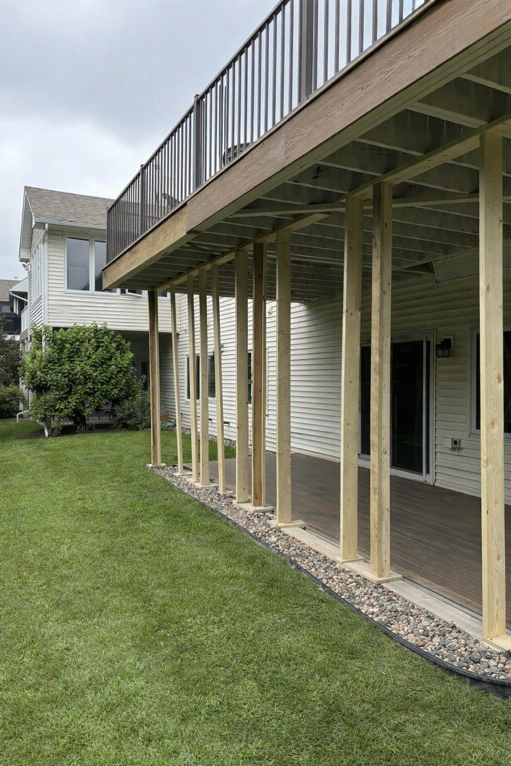 Person working on landscaping beside a house, with tools, gravel, and a ladder on the lawn.