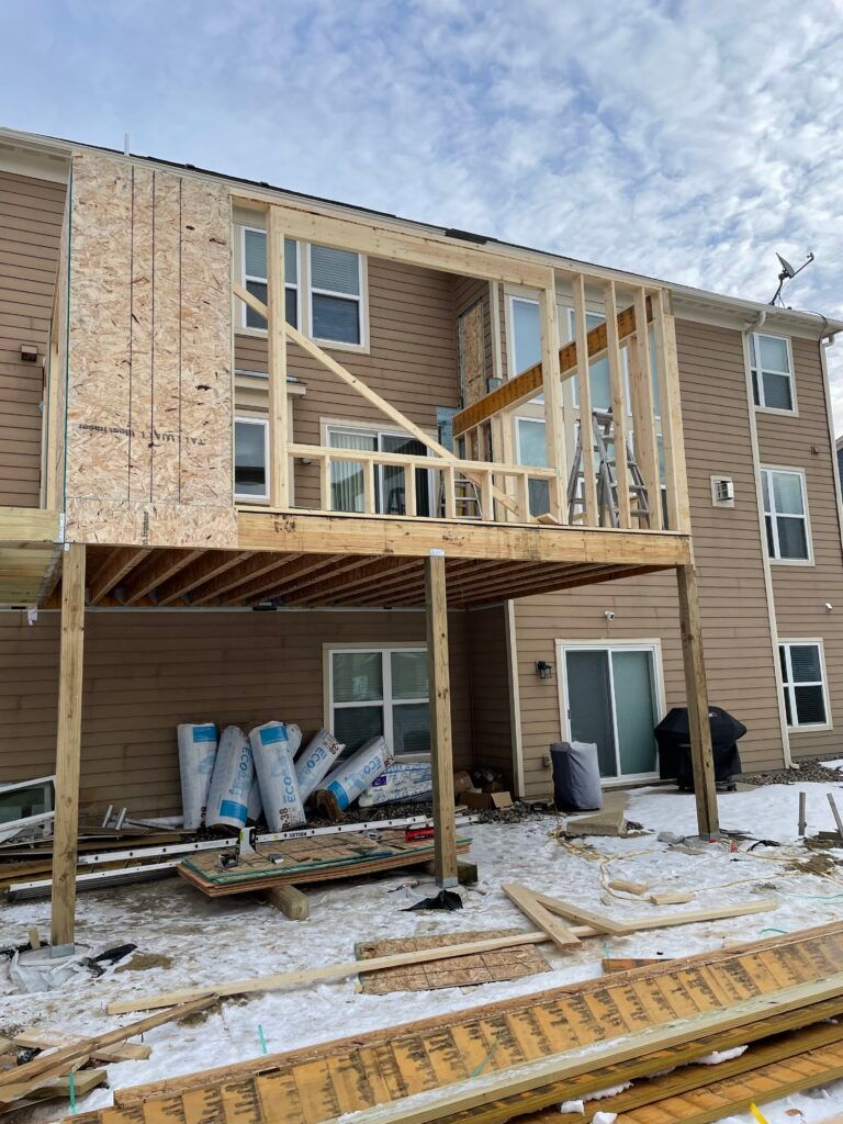 Apartment building under renovation with new wooden framing on second-floor balcony and construction materials below