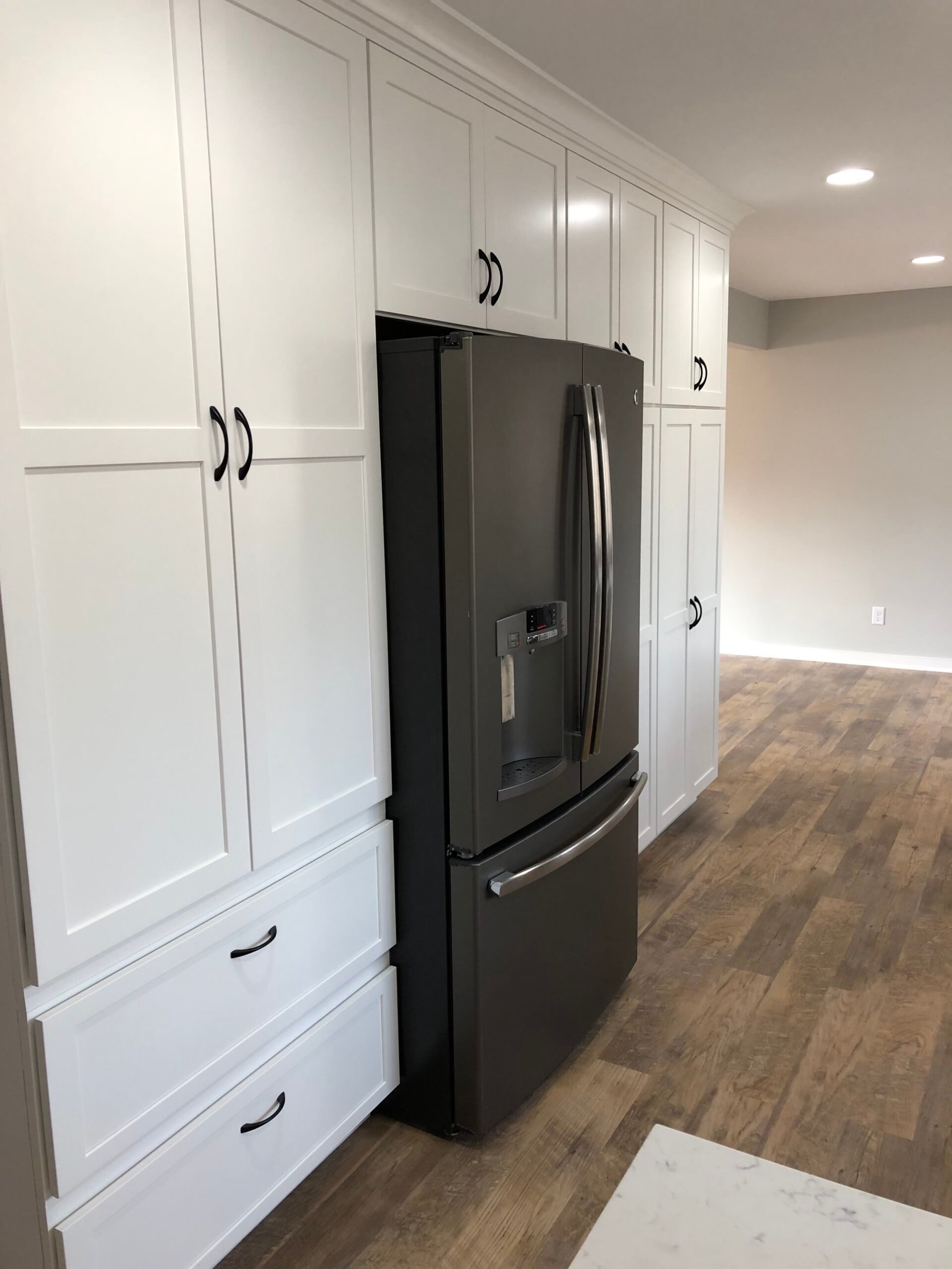 White kitchen with built-in cabinets, black refrigerator, and wood-look flooring along a bright hallway