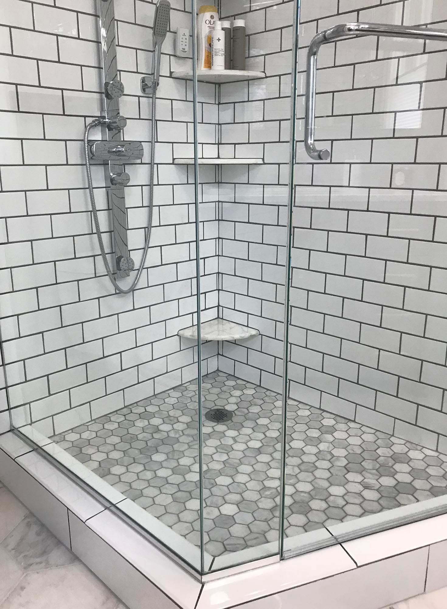 Glass shower stall with white subway tile and hexagon floor tile, showing chrome fixtures and shelves