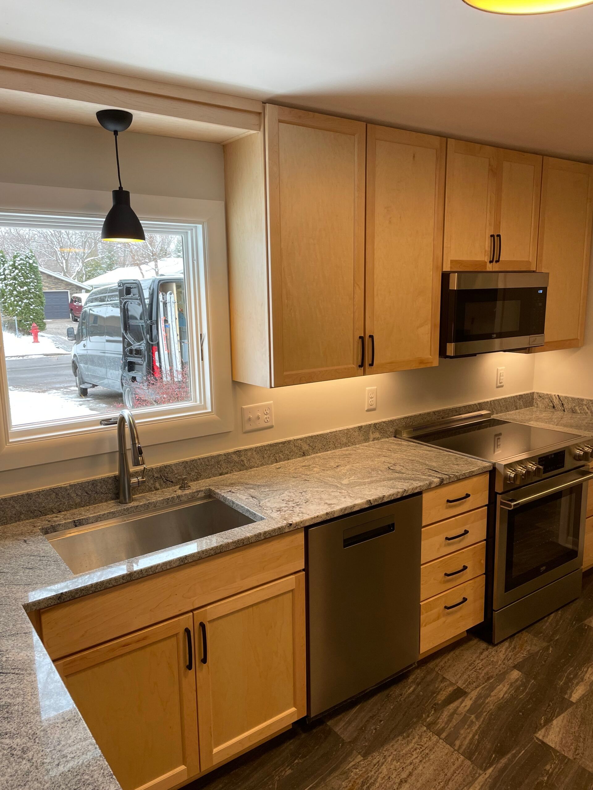 Kitchen with light wood cabinets, granite countertops, stainless appliances, and a window over the sink.