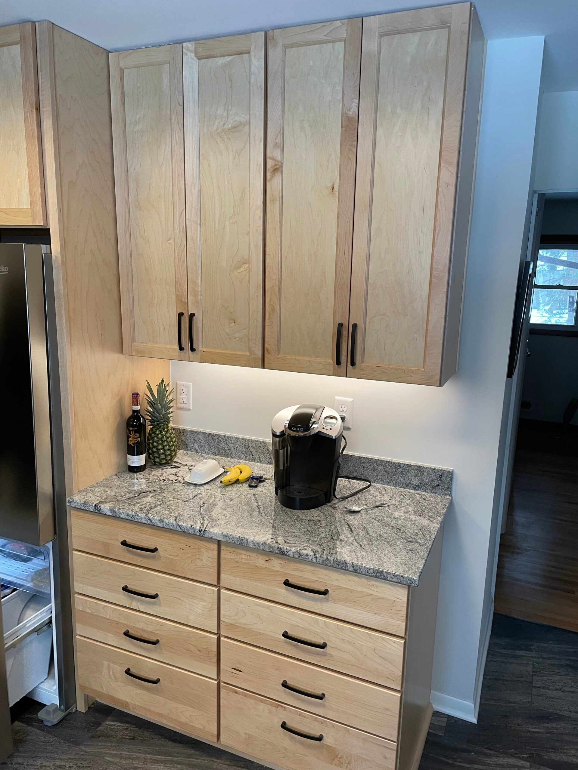 Kitchen counter and cabinets with granite top, light wood drawers, and a black coffee maker.