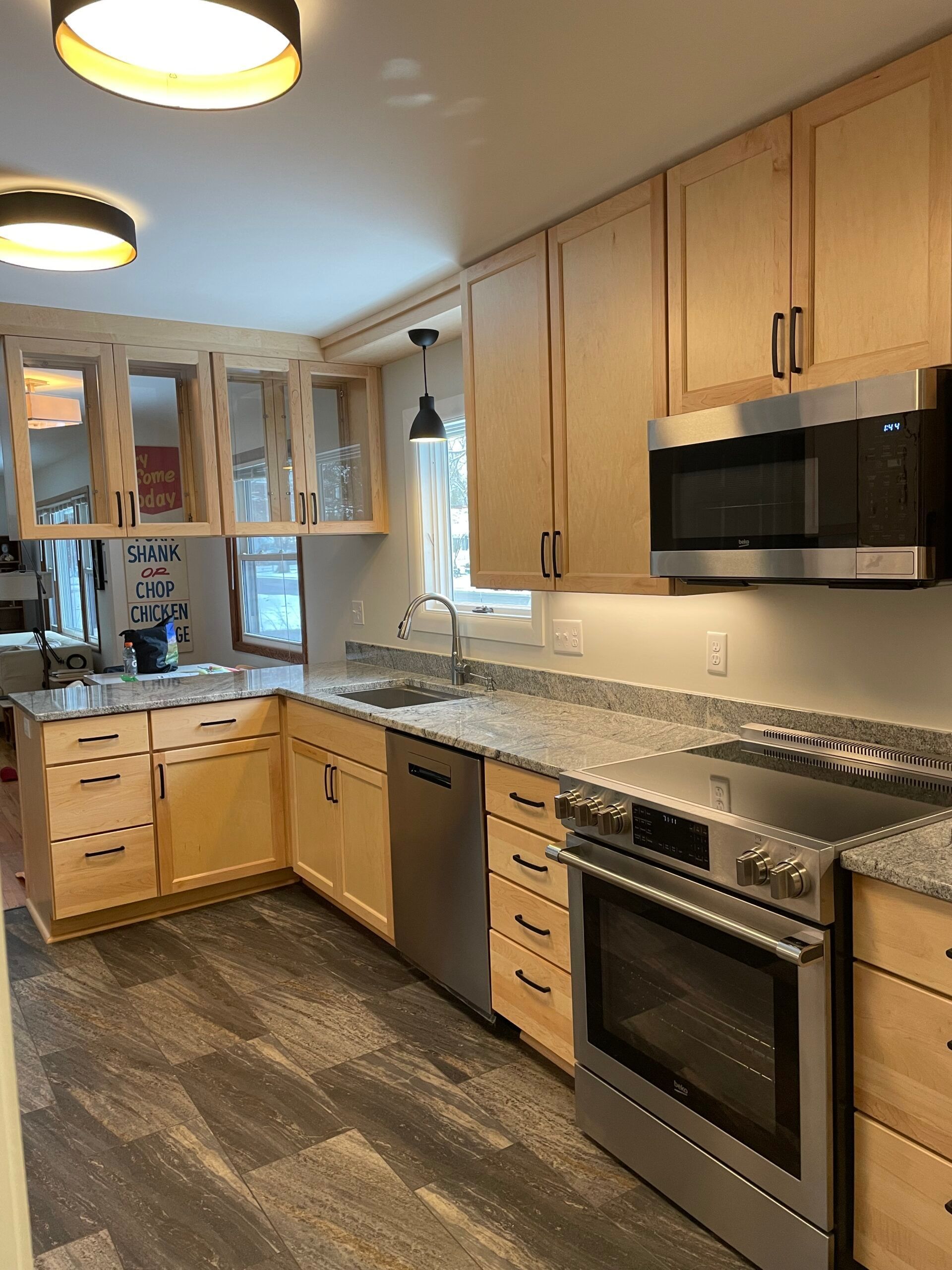 Modern kitchen with light wood cabinets, granite counters, stainless appliances, and patterned flooring.