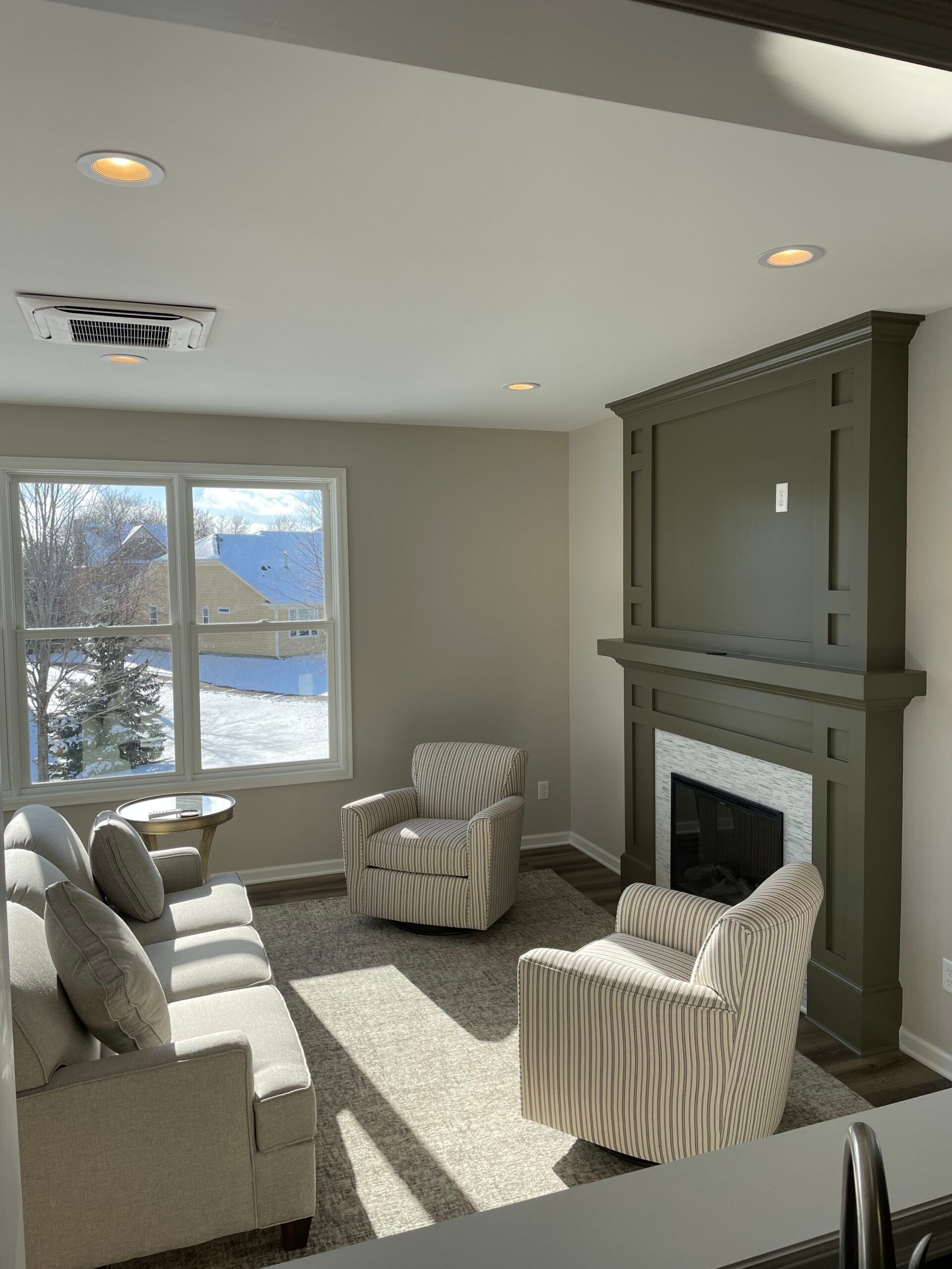Bright living room with gray furniture, striped chairs, a fireplace, and large sunlit windows