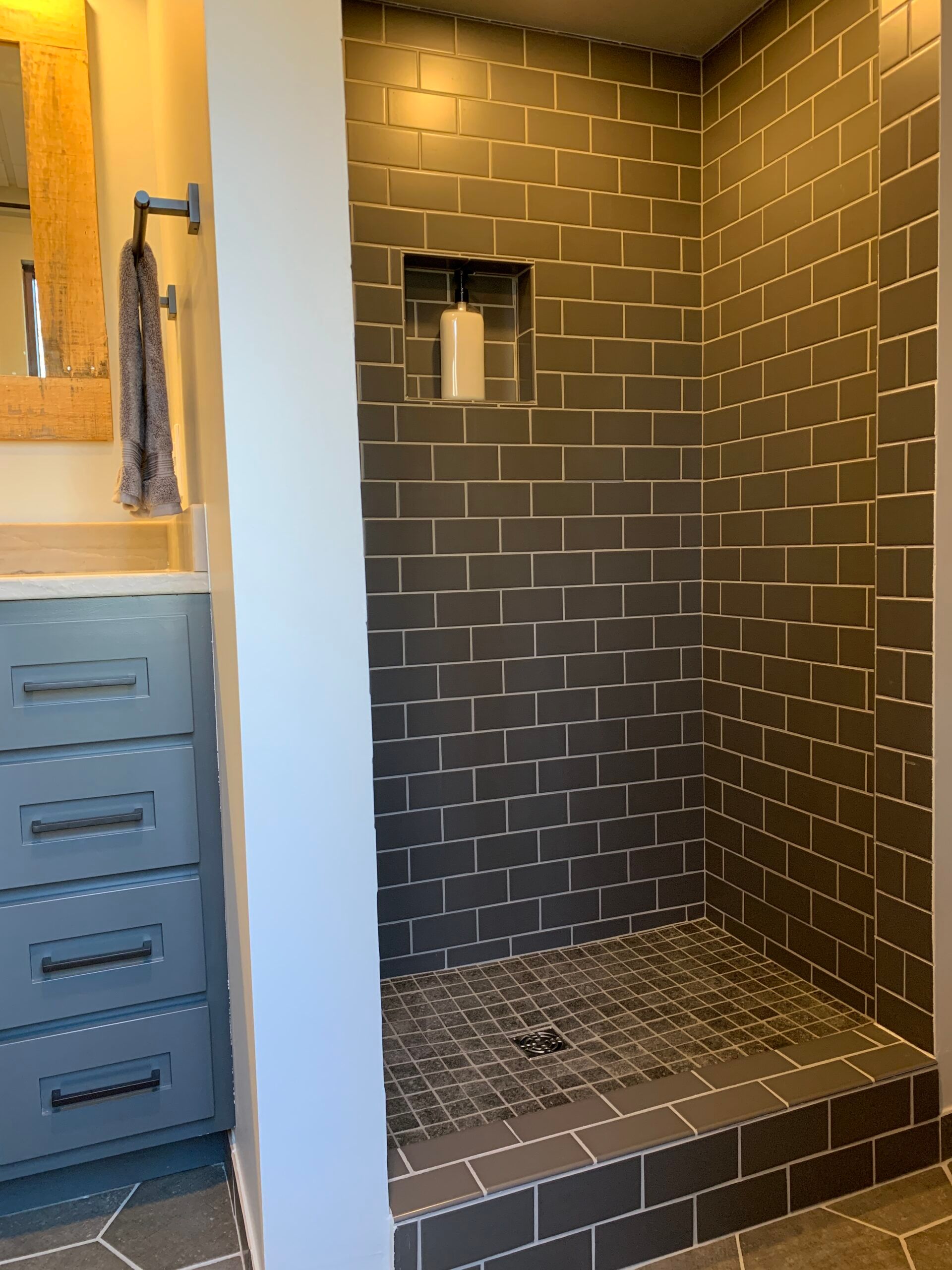 Tiled walk-in shower with dark brick walls, small window, and built-in bench next to a vanity cabinet
