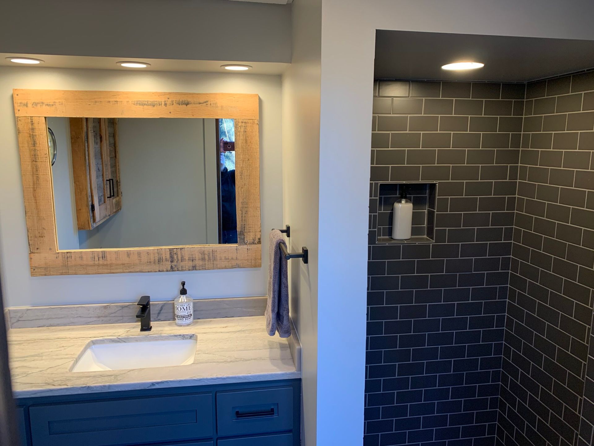 Bathroom vanity with sink and mirror beside a black-tiled shower