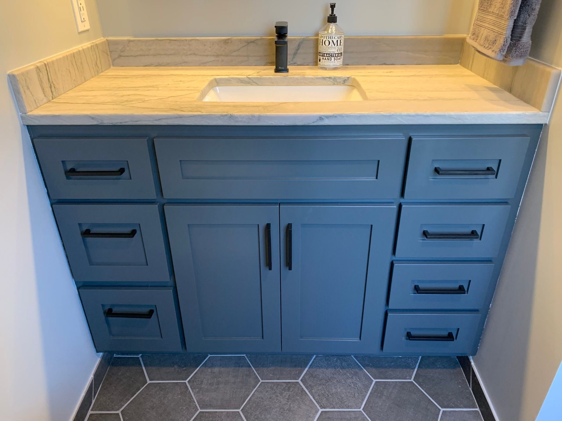 Blue bathroom vanity with gray countertop, white sink, and hex tile floor