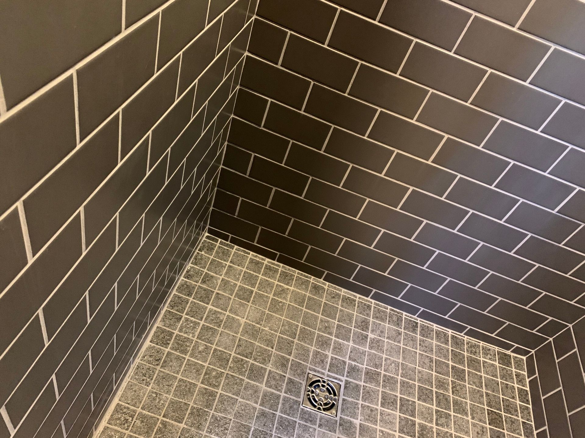 Small tiled shower corner with dark walls, light floor tiles, and a drain.