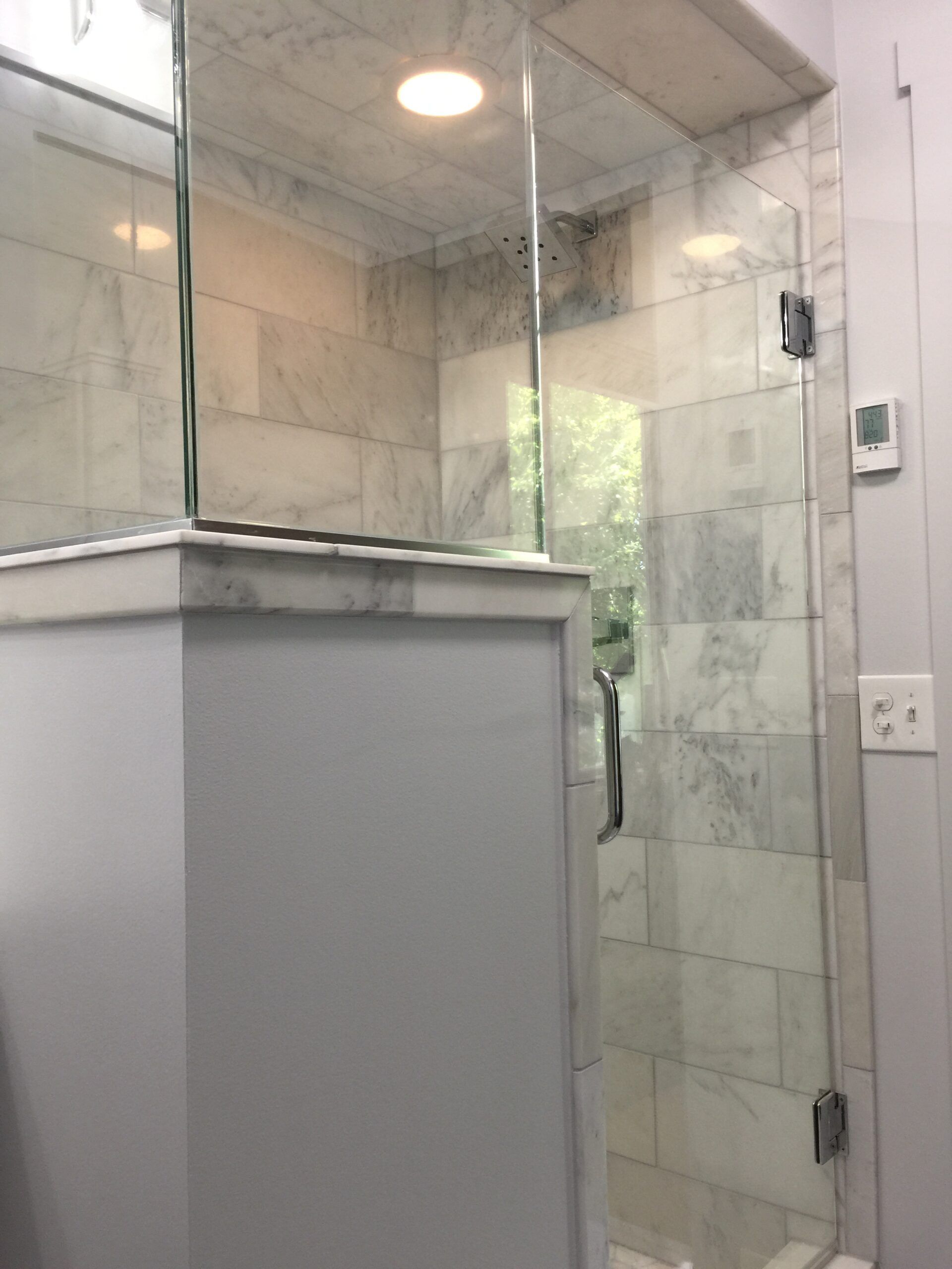 Glass shower stall with tiled walls and a half-height partition in a bathroom.