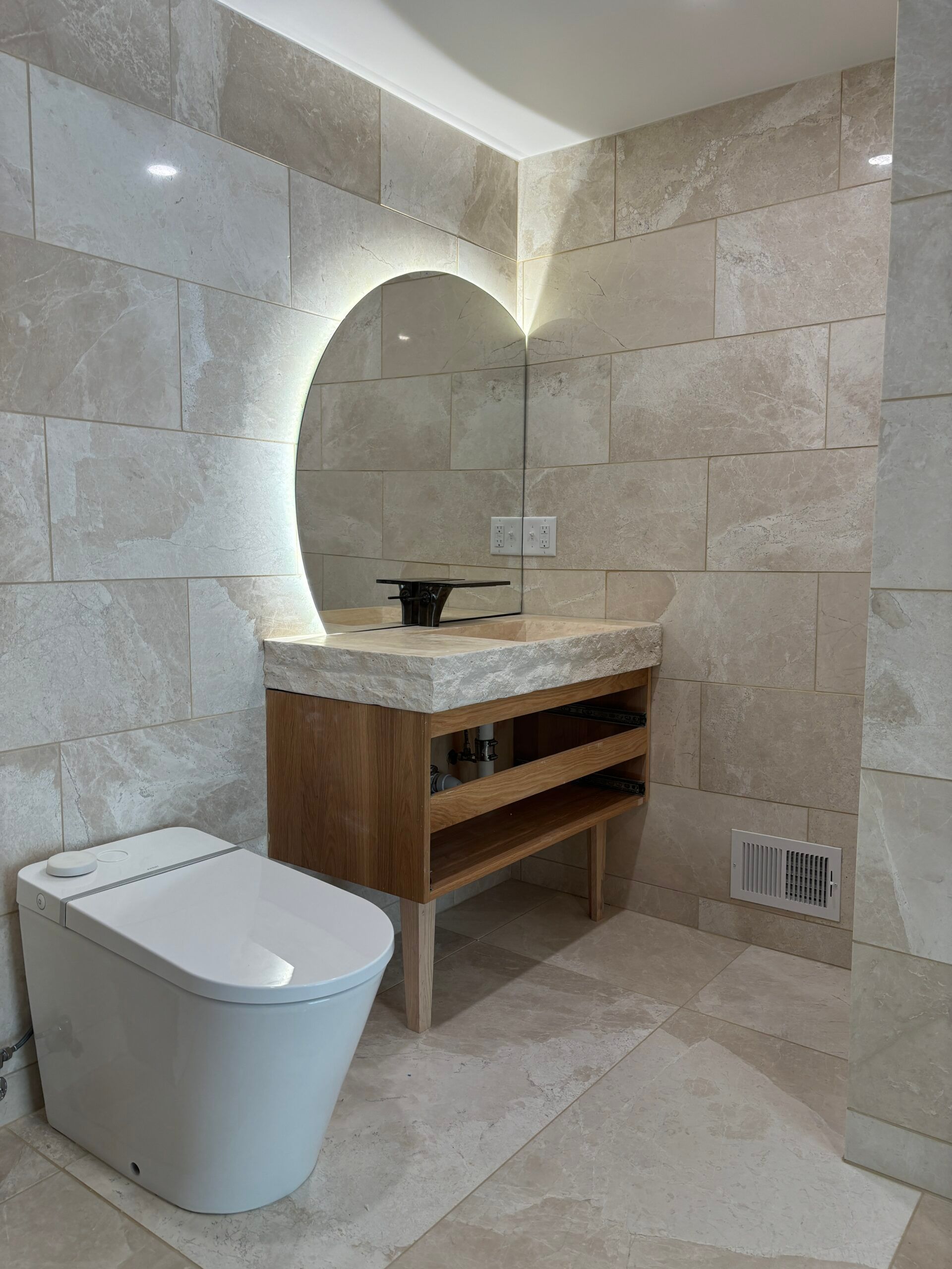 Modern bathroom with toilet, stone sink vanity, and arched illuminated mirror window