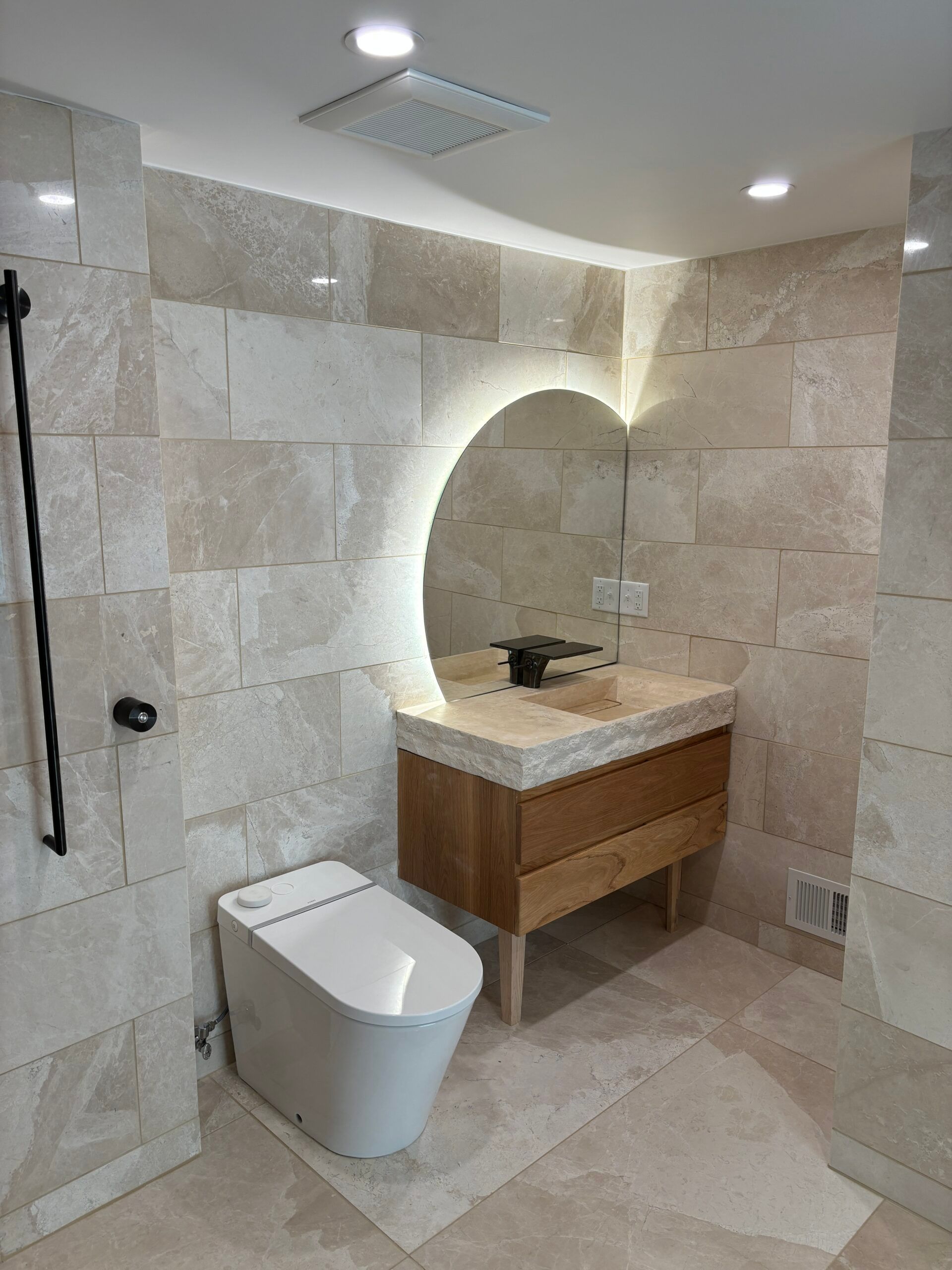 Modern beige bathroom with toilet, wooden vanity, mirror, and walk-in shower with grab bar