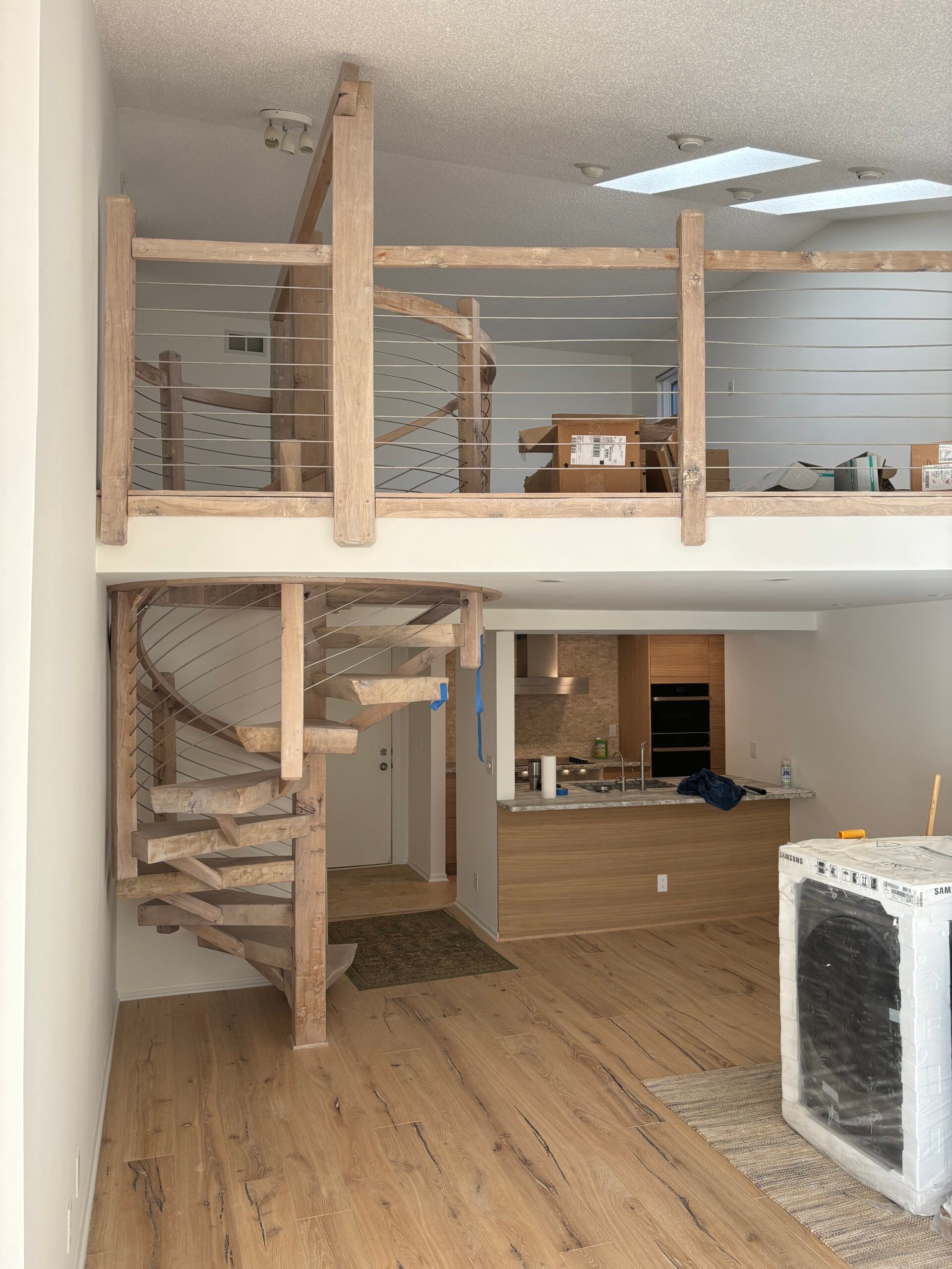 Interior under construction with a wooden spiral staircase and mezzanine overlooking an open room