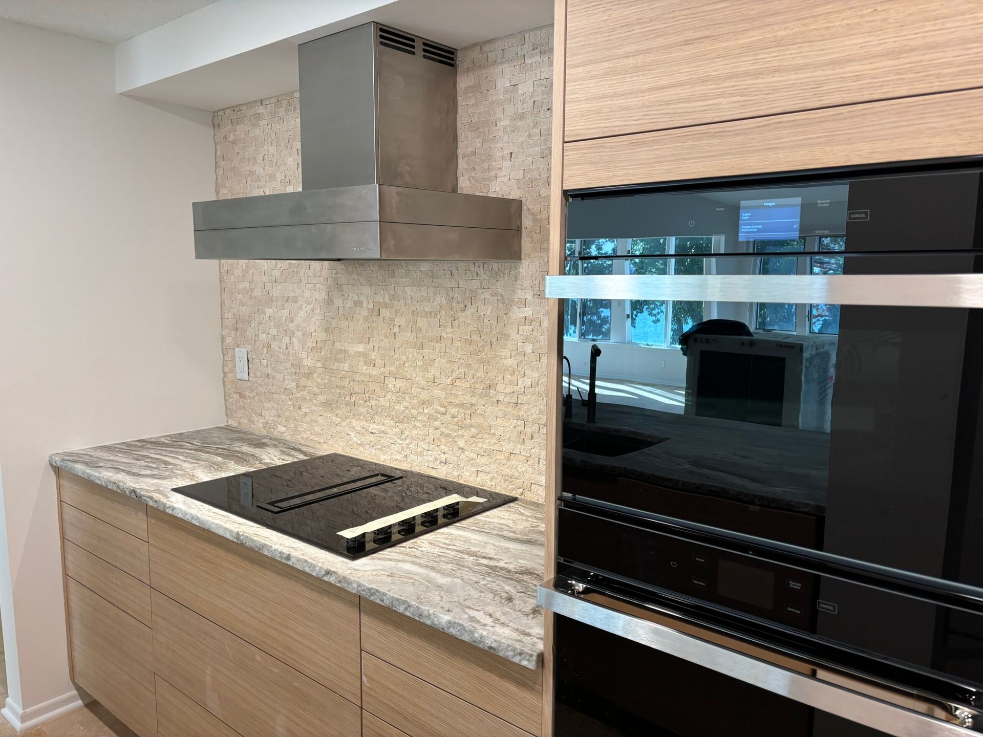 Modern kitchen with marble countertops, cooktop, range hood, and built-in double oven