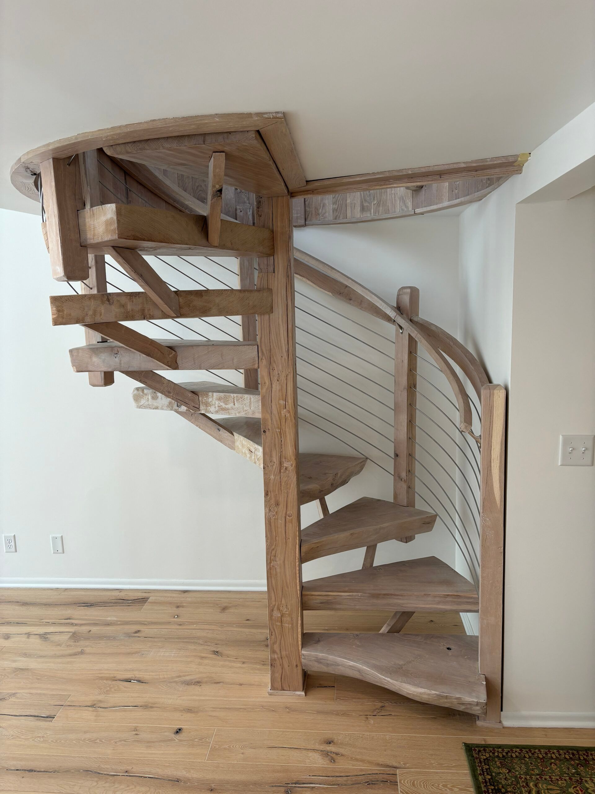 Curved wooden spiral staircase in a bright room with white walls and hardwood floor