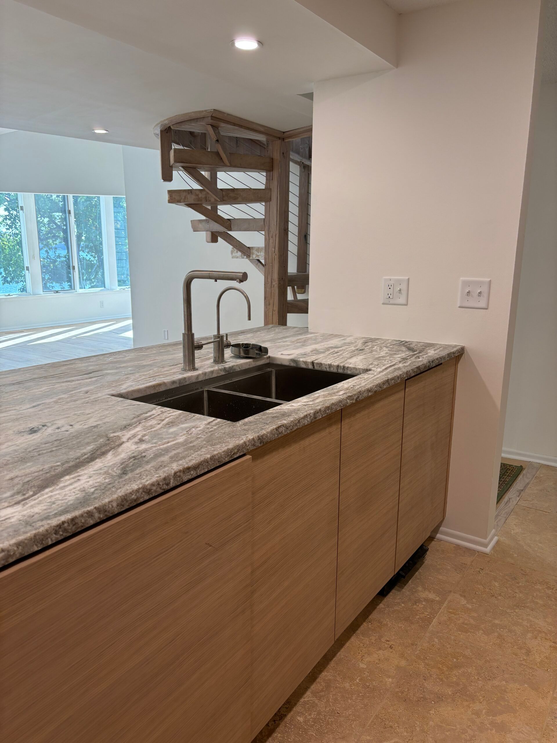 Modern kitchen with granite island, stainless sink, and staircase in the background