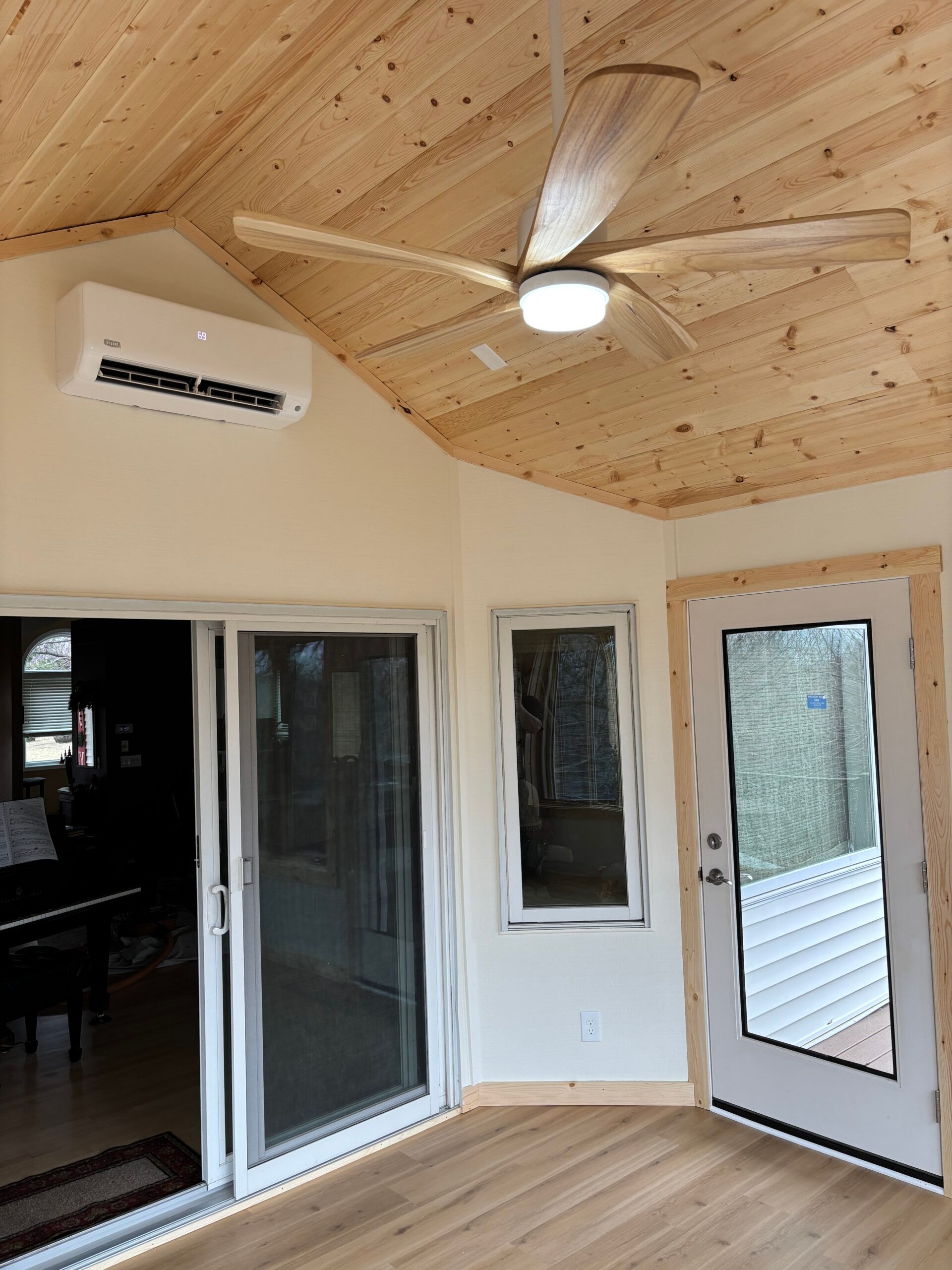 Enclosed porch with pine ceiling, ceiling fan, sliding glass door, and exterior door with deck railing view.