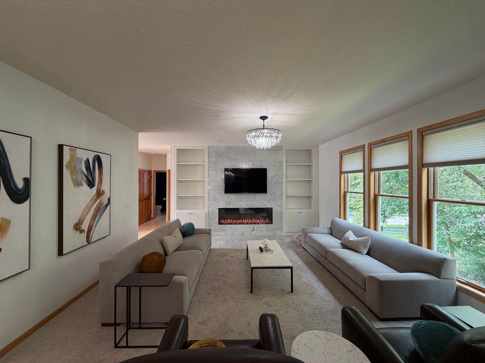 Bright modern living room with gray sofas, wall art, TV above fireplace, and large windows.