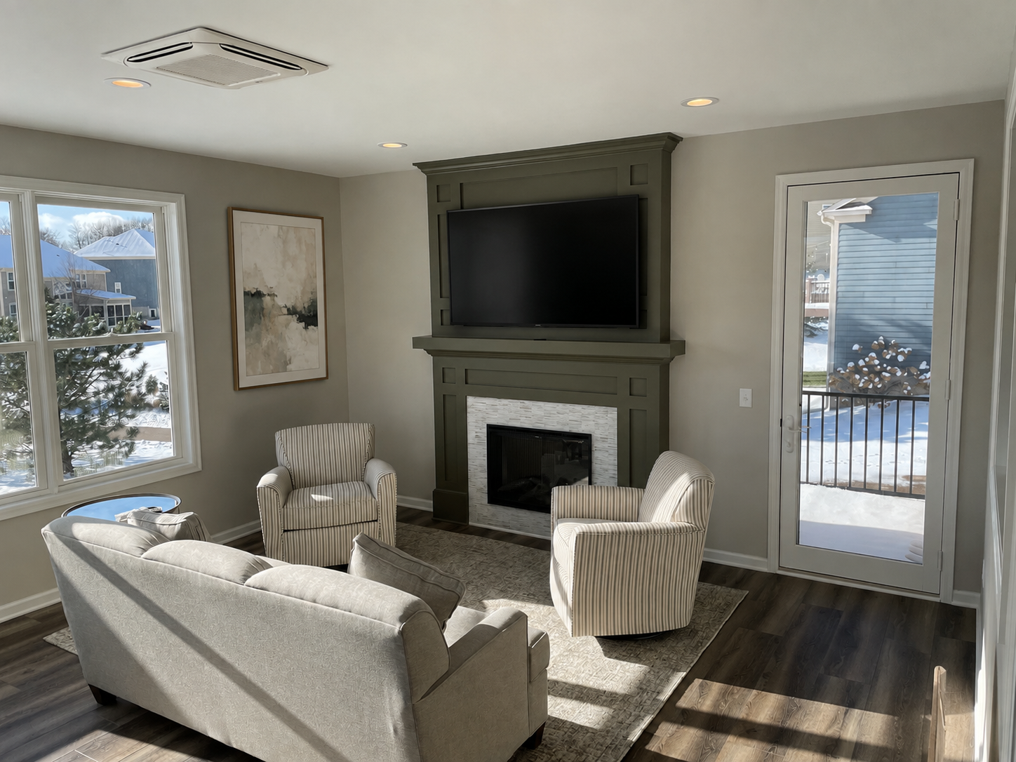 Bright living room with green fireplace, beige armchairs, sofa, and large window with snowy view