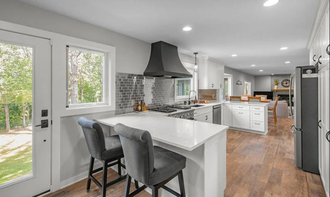 Modern open kitchen with white island, bar stools, gray hood, wood floors, and bright windows Modern open kitchen with white island, bar stools, gray hood, wood floors, and bright windows