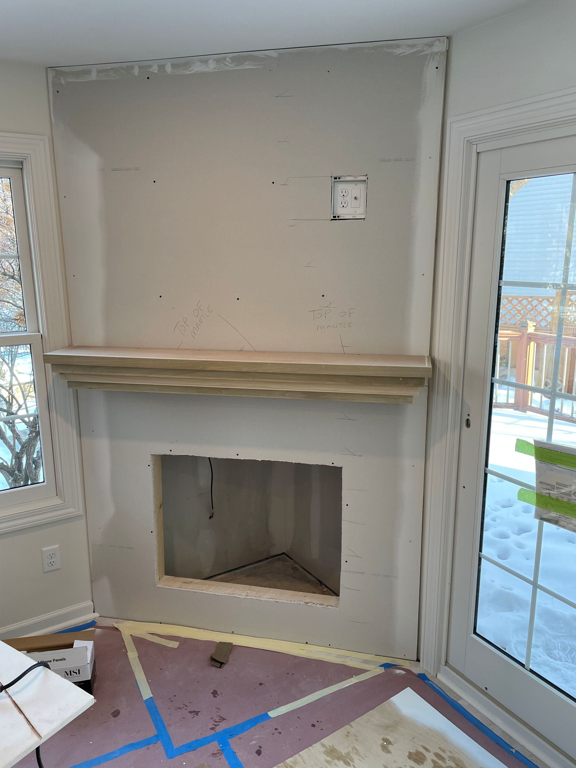 Empty room with a fireplace and mantel, white walls, windows, and blue painter’s tape on the floor.