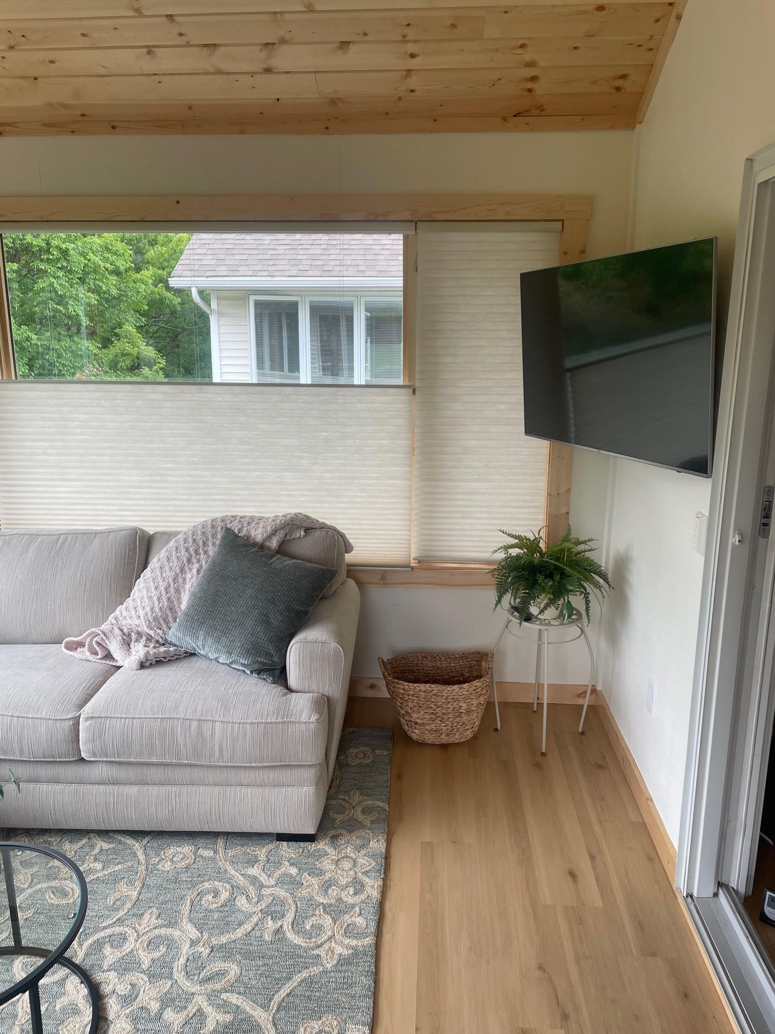 Cozy sunroom with gray sofa, wall-mounted TV, woven basket, and light wood walls and floor