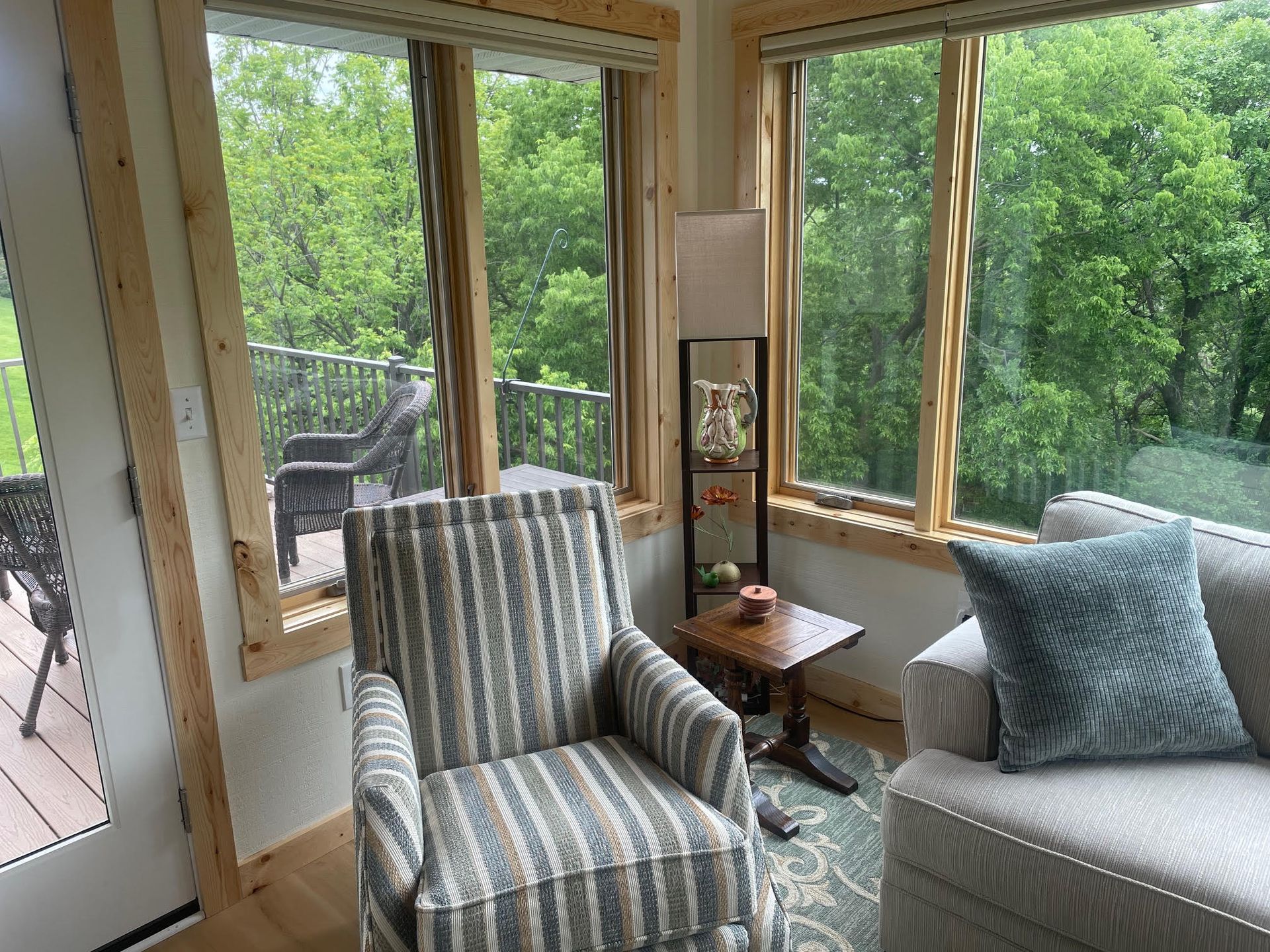 Sunroom with striped armchair, sofa, side table, and large windows overlooking green trees
