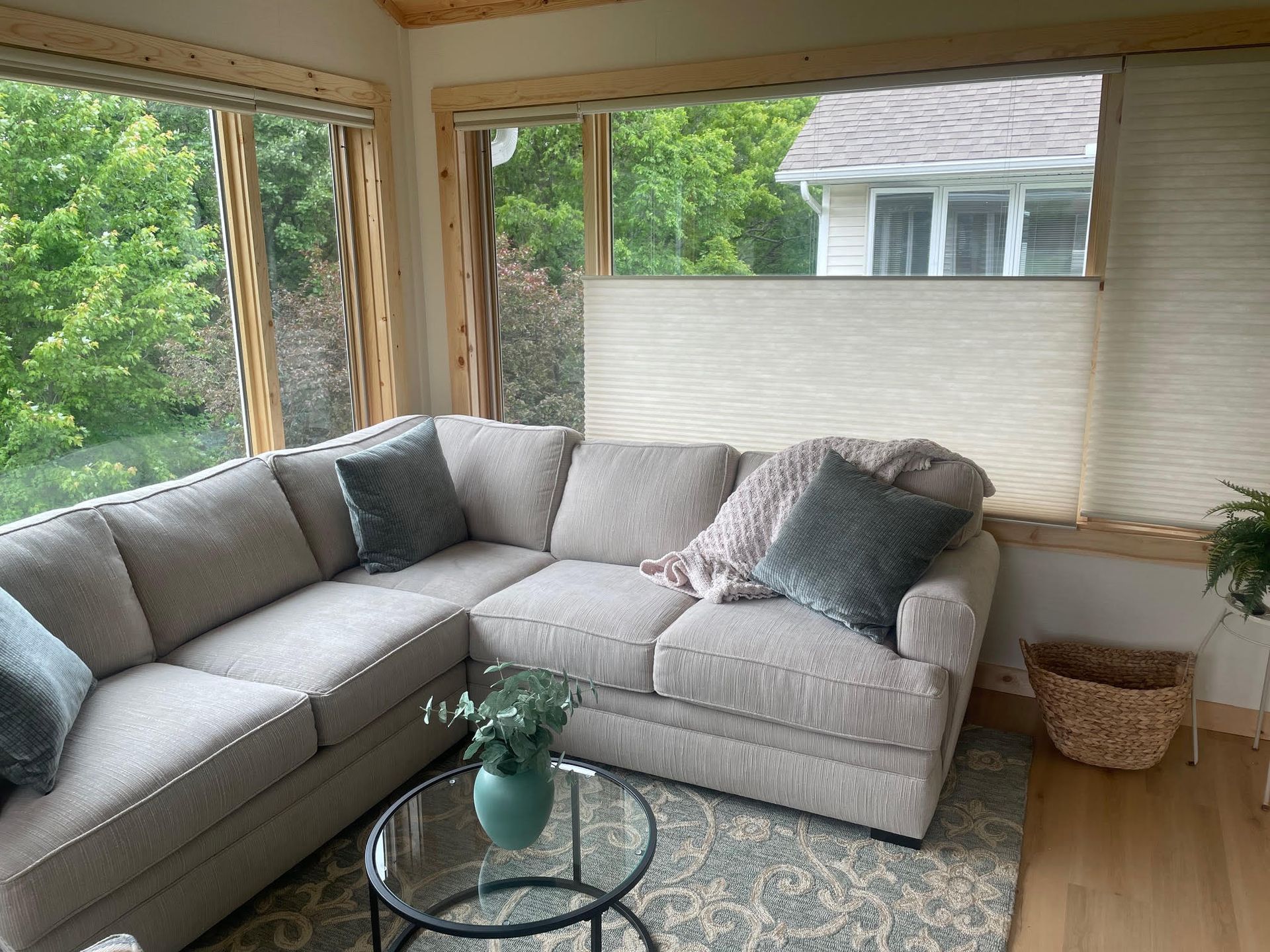 Bright living room with gray sectional sofa, glass coffee table, large windows, and green outdoor view