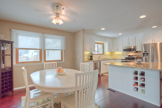 Bright kitchen and dining area with white table, cabinets, granite island, and large windows Bright kitchen and dining area with white table, cabinets, granite island, and large windows