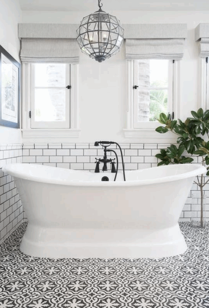 Black-and-white bathroom with a freestanding tub, patterned floor, windows, and hanging pendant light