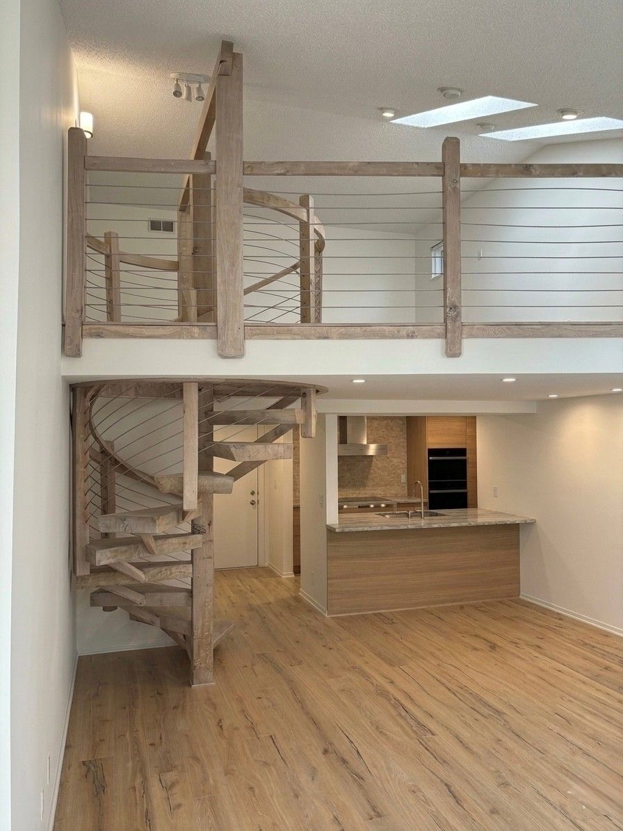 Curved wooden spiral staircase in a bright room with white walls and hardwood floor