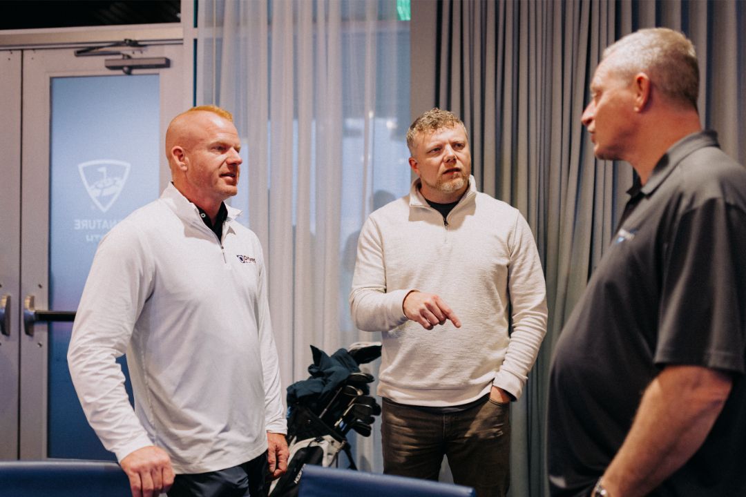 Three men are standing in a room talking to each other.