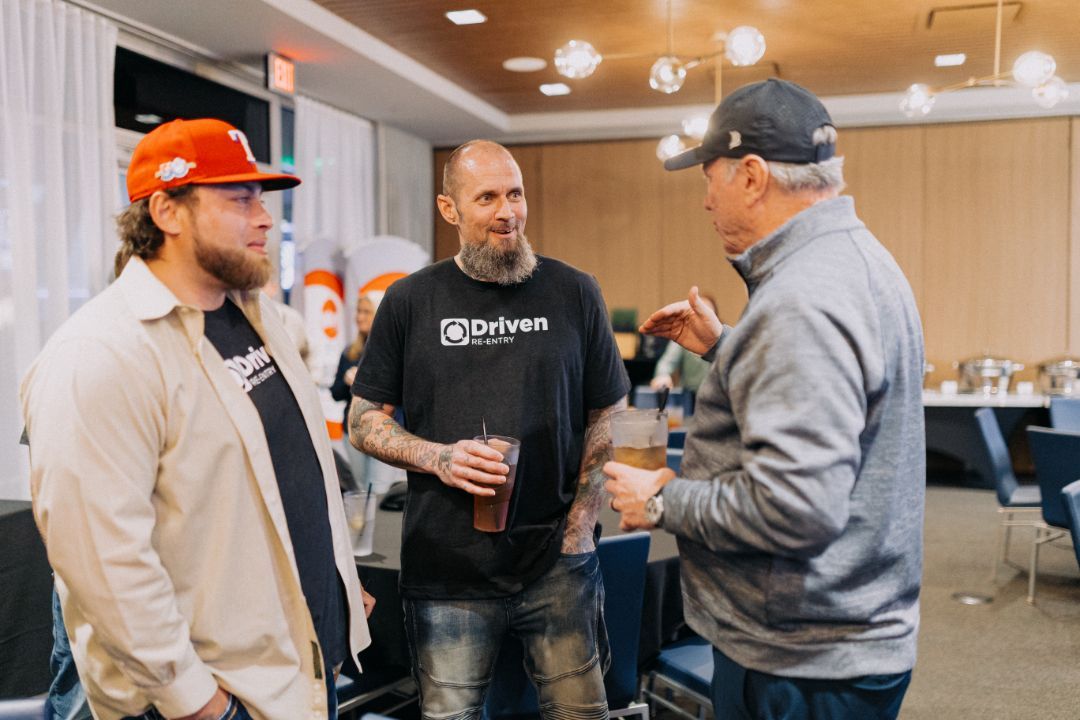 Three men are standing in a room talking to each other.
