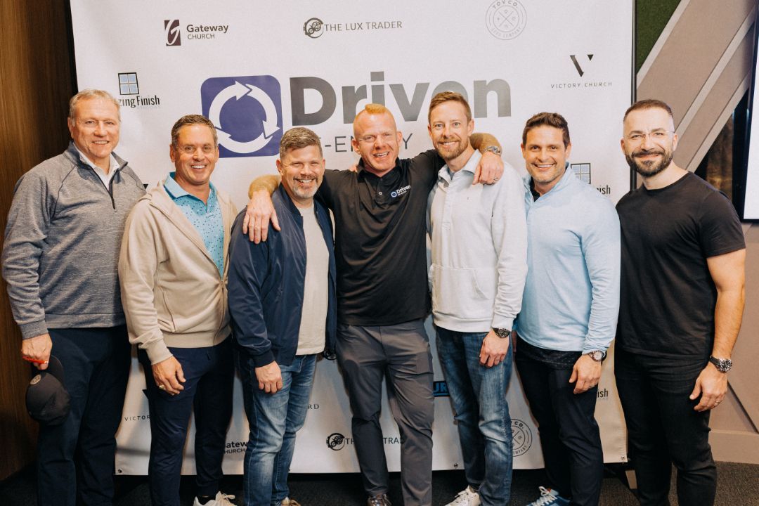 A group of men are posing for a picture in front of a sign that says driven energy.