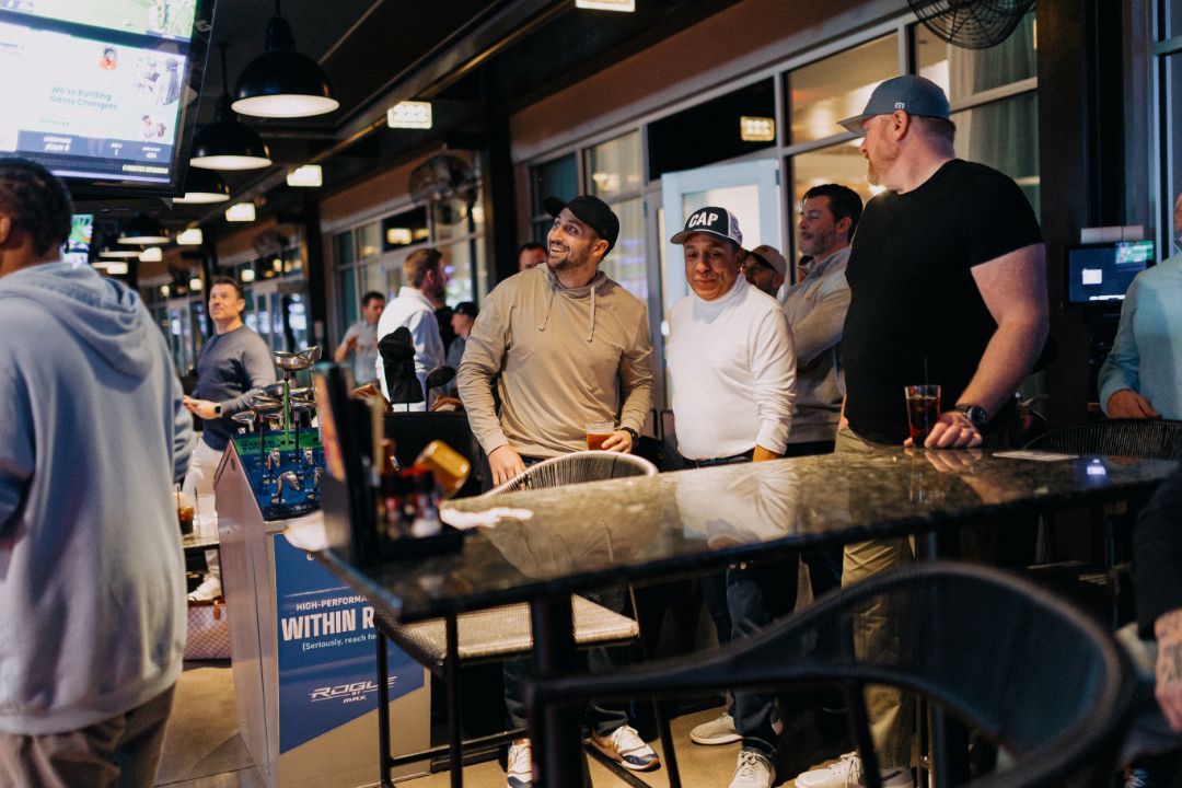 A group of men are standing around tables in a restaurant.