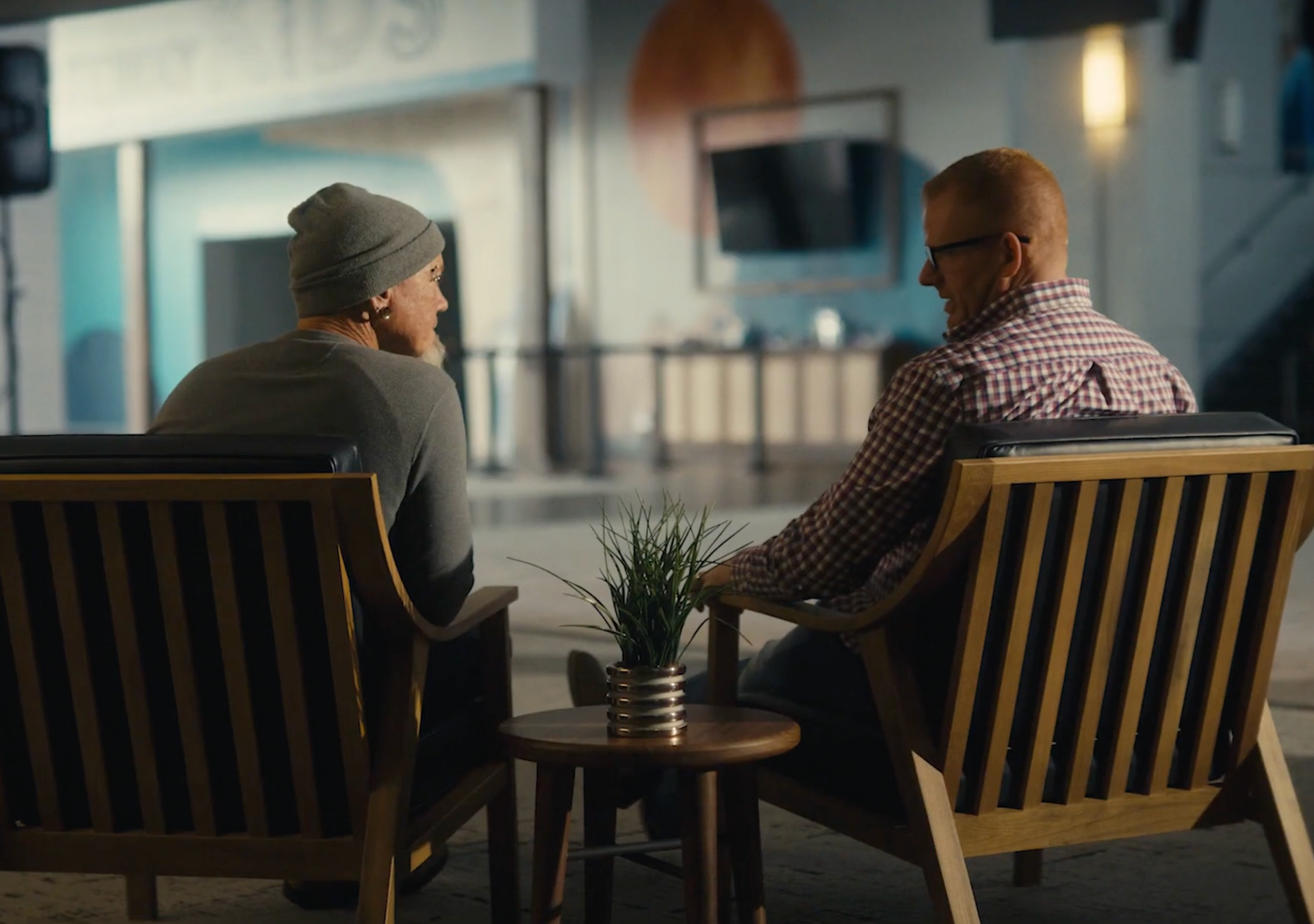 Two men are sitting in chairs talking to each other.