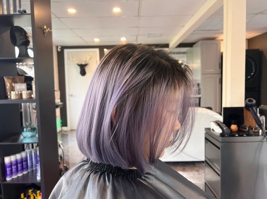 A woman with purple hair is getting her hair cut in a salon.