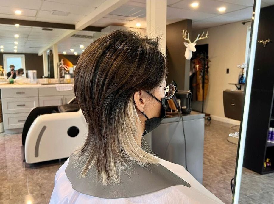 A woman wearing a mask is getting her hair dyed in a salon.