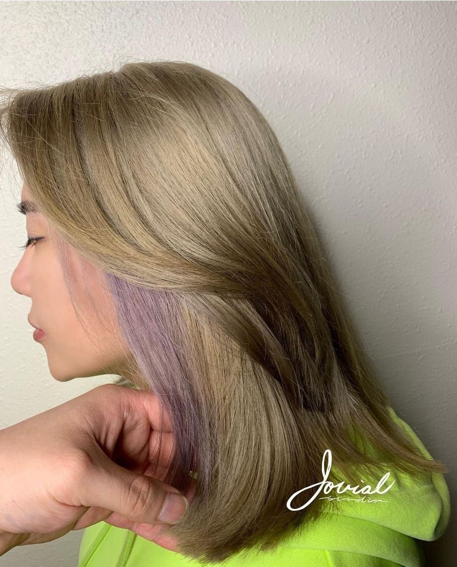 A woman with blonde hair and purple highlights is getting her hair dyed.